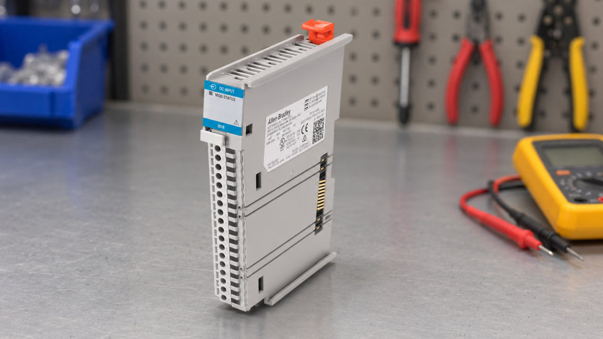 Allen-Bradley 5069-IB16 input module standing on a steel workbench next to a multimeter, pliers and a screwdriver